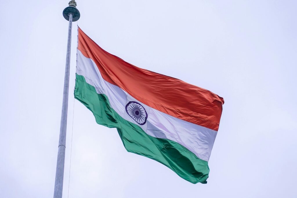 The Indian national flag proudly waves on a flagpole against a clear blue sky in Noida, India.