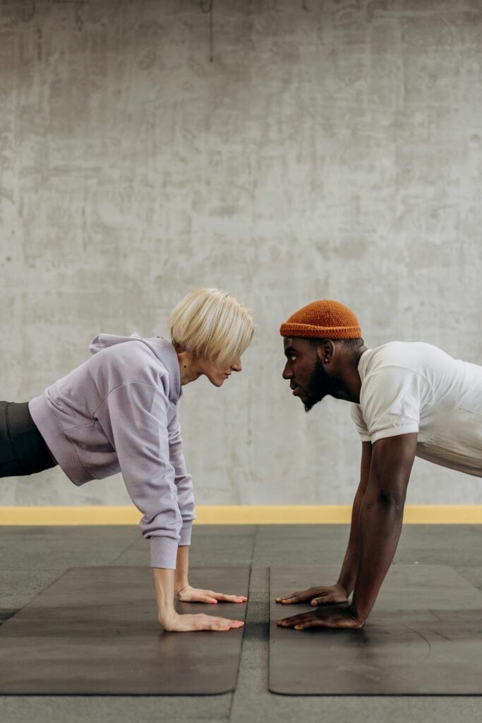Two adults face off in a plank exercise on gym mats, embodying fitness and diversity.